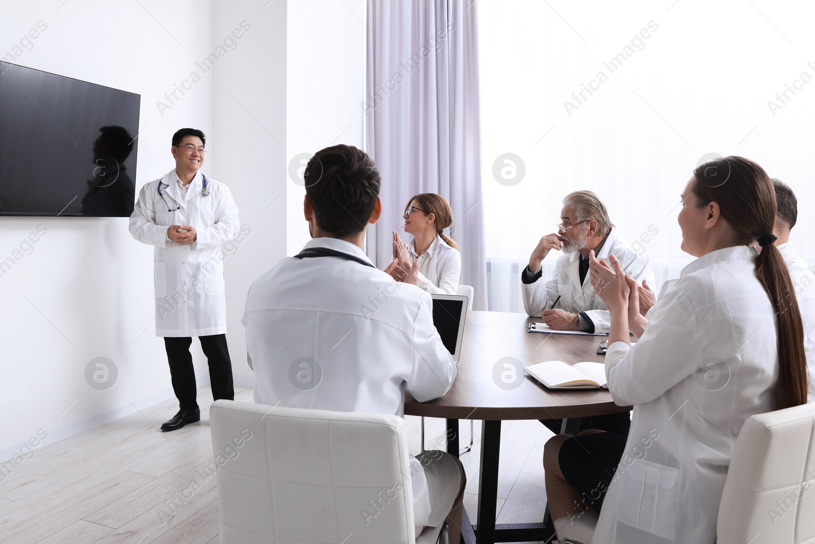 Team of doctors listening to speaker report near tv screen in meeting room. Medical conference Photo of Team of doctors listening to speaker report near tv screen in meeting room. Medical conference