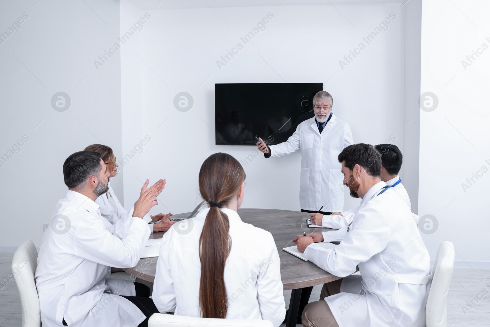 Team of doctors listening to senior speaker report near tv screen in meeting room. Medical conference Photo of Team of doctors listening to senior speaker report near tv screen in meeting room. Medical conference