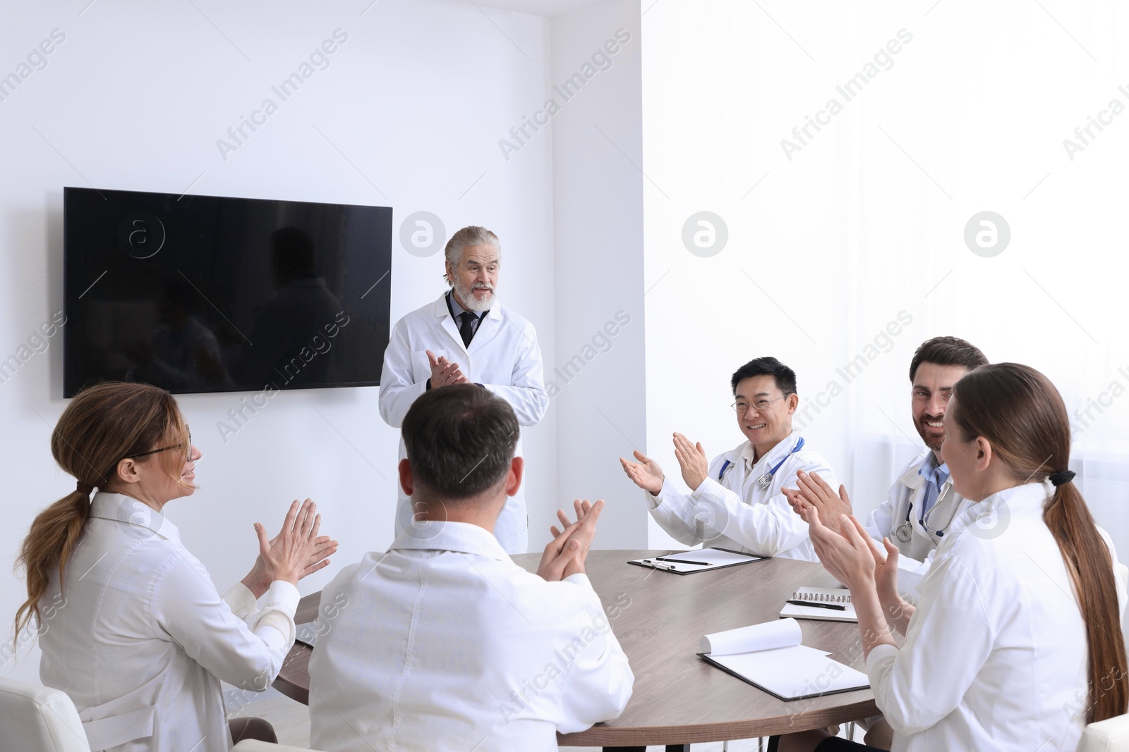 Team of doctors listening to senior speaker report near tv screen in meeting room. Medical conference Photo of Team of doctors listening to senior speaker report near tv screen in meeting room. Medical conference