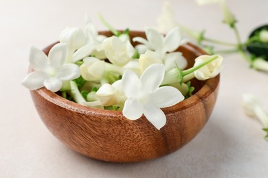 Photo of Bowl with jasmine flowers on beige table, closeup