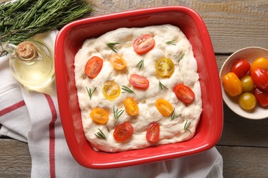Photo of Raw focaccia with tomatoes, rosemary and oil on wooden table, flat lay