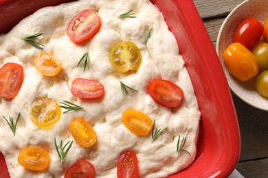 Photo of Raw focaccia with tomatoes and rosemary on wooden table, flat lay