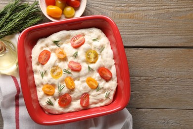 Photo of Raw focaccia with tomatoes, rosemary and oil on wooden table, flat lay. Space for text