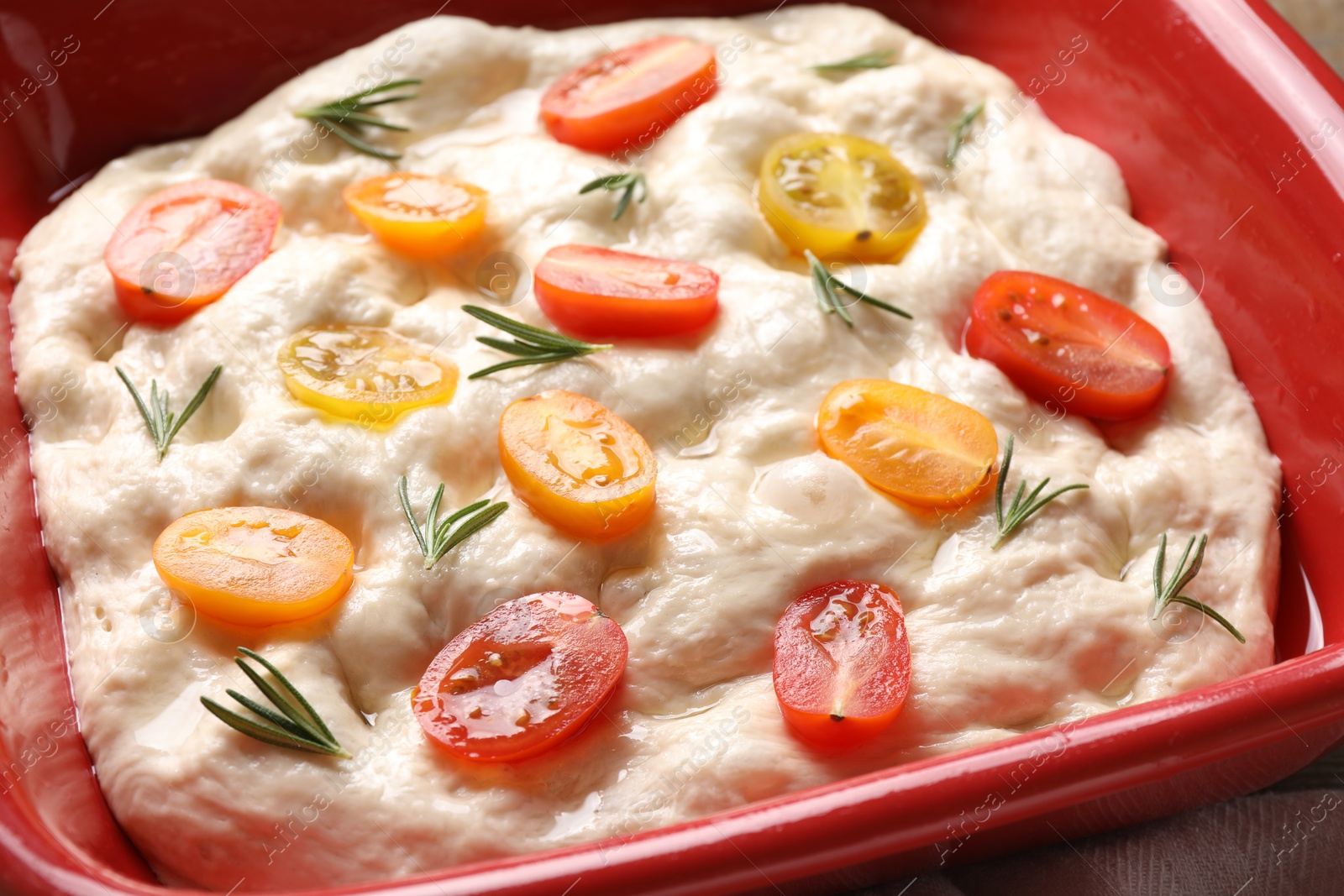 Raw focaccia with tomatoes and rosemary in baking dish on table, closeup Photo of Raw focaccia with tomatoes and rosemary in baking dish on table, closeup