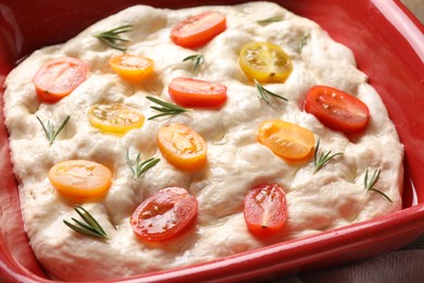 Photo of Raw focaccia with tomatoes and rosemary in baking dish on table, closeup