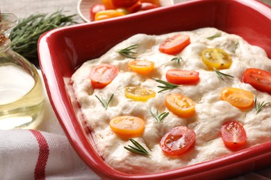 Photo of Raw focaccia with tomatoes, rosemary and oil on table, closeup
