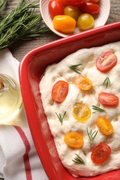 Photo of Raw focaccia with tomatoes, rosemary and oil on table, flat lay