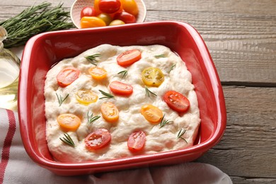 Photo of Raw focaccia with tomatoes, rosemary and oil on wooden table, closeup