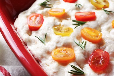 Photo of Raw focaccia with tomatoes and rosemary in baking dish on table, closeup