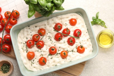 Photo of Raw focaccia with tomatoes and spices on light textured table, flat lay