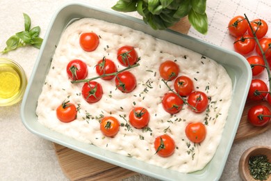 Photo of Raw focaccia with tomatoes and spices on light textured table, flat lay