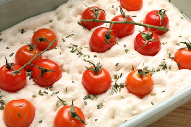 Photo of Raw focaccia with tomatoes and rosemary in baking dish on table, closeup
