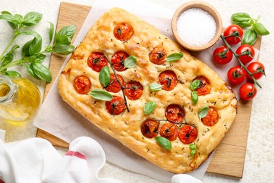 Photo of Delicious focaccia with tomatoes, spices and oil on beige table, flat lay