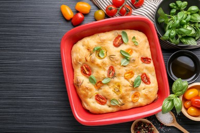 Photo of Delicious focaccia with tomatoes, spices and oil on black wooden table, flat lay