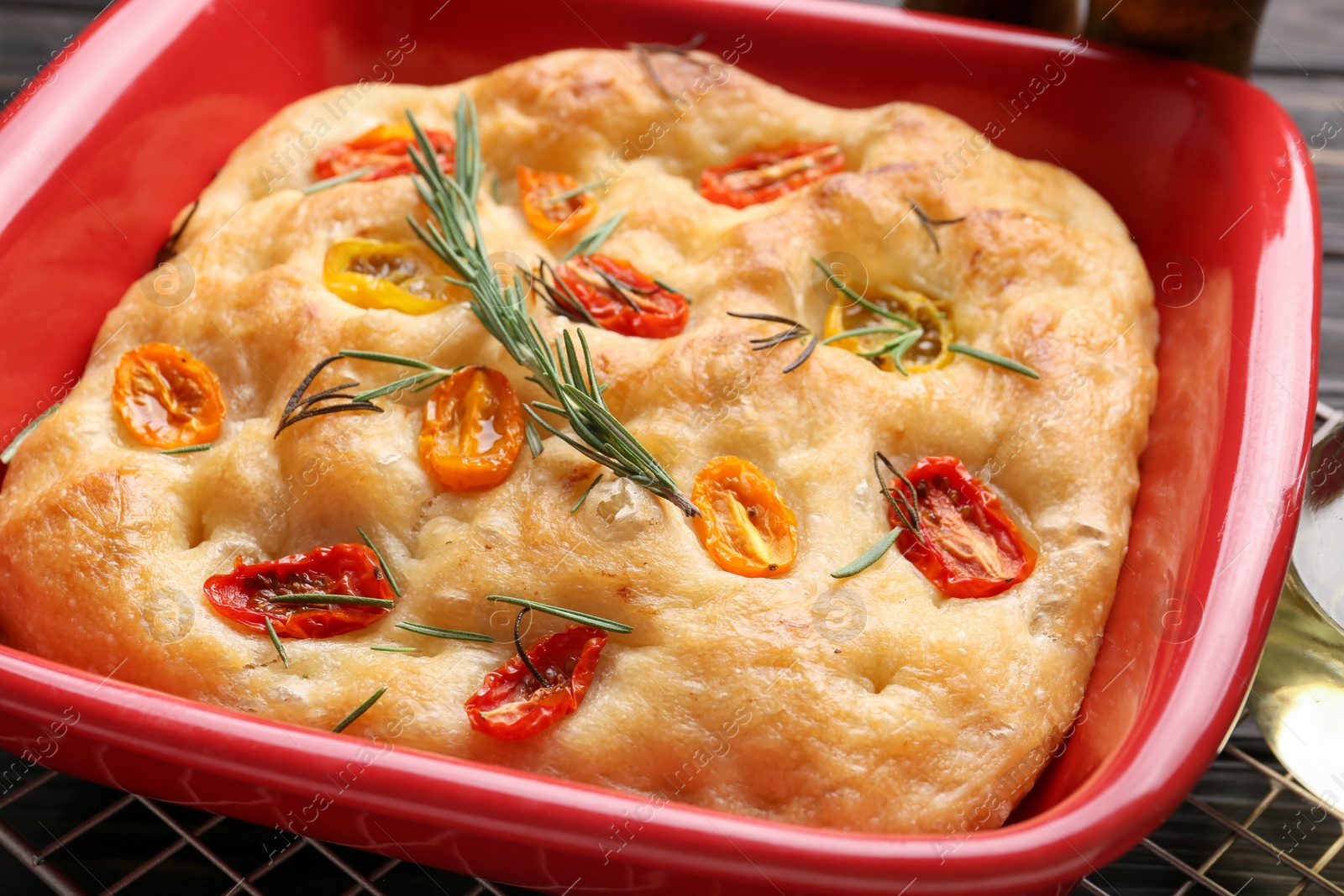 Delicious focaccia with tomatoes and rosemary in baking dish on table, closeup Photo of Delicious focaccia with tomatoes and rosemary in baking dish on table, closeup