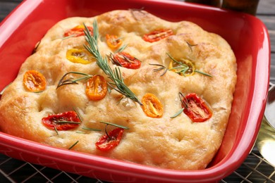 Photo of Delicious focaccia with tomatoes and rosemary in baking dish on table, closeup