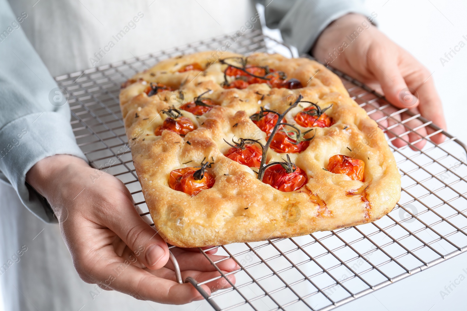Woman holding delicious focaccia with tomatoes and spices on light background, closeup Photo of Woman holding delicious focaccia with tomatoes and spices on light background, closeup
