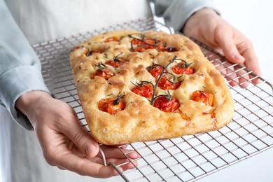 Photo of Woman holding delicious focaccia with tomatoes and spices on light background, closeup