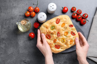 Photo of Woman with delicious focaccia with tomatoes, spices and oil at gray textured table, top view
