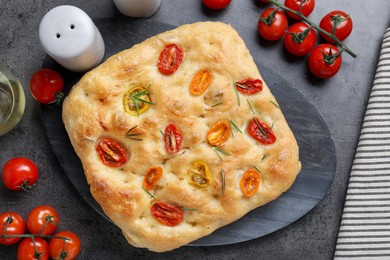 Photo of Delicious focaccia with tomatoes, spices and oil on gray table, flat lay