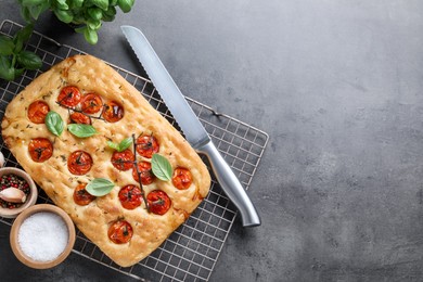 Photo of Delicious focaccia with tomatoes, spices and knife on gray textured table, flat lay. Space for text