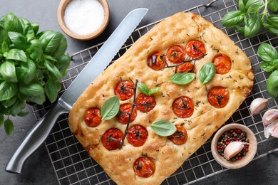 Photo of Delicious focaccia with tomatoes, spices and knife on gray table, flat lay