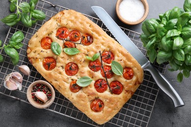 Photo of Delicious focaccia with tomatoes, spices and knife on gray textured table, flat lay