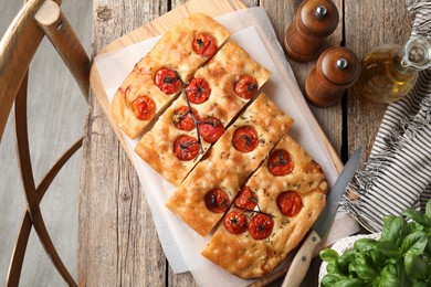 Photo of Cut delicious focaccia with tomatoes, spices and oil on wooden table, flat lay