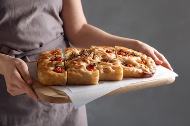 Photo of Woman holding cut delicious focaccia with tomatoes and spices on gray background, closeup