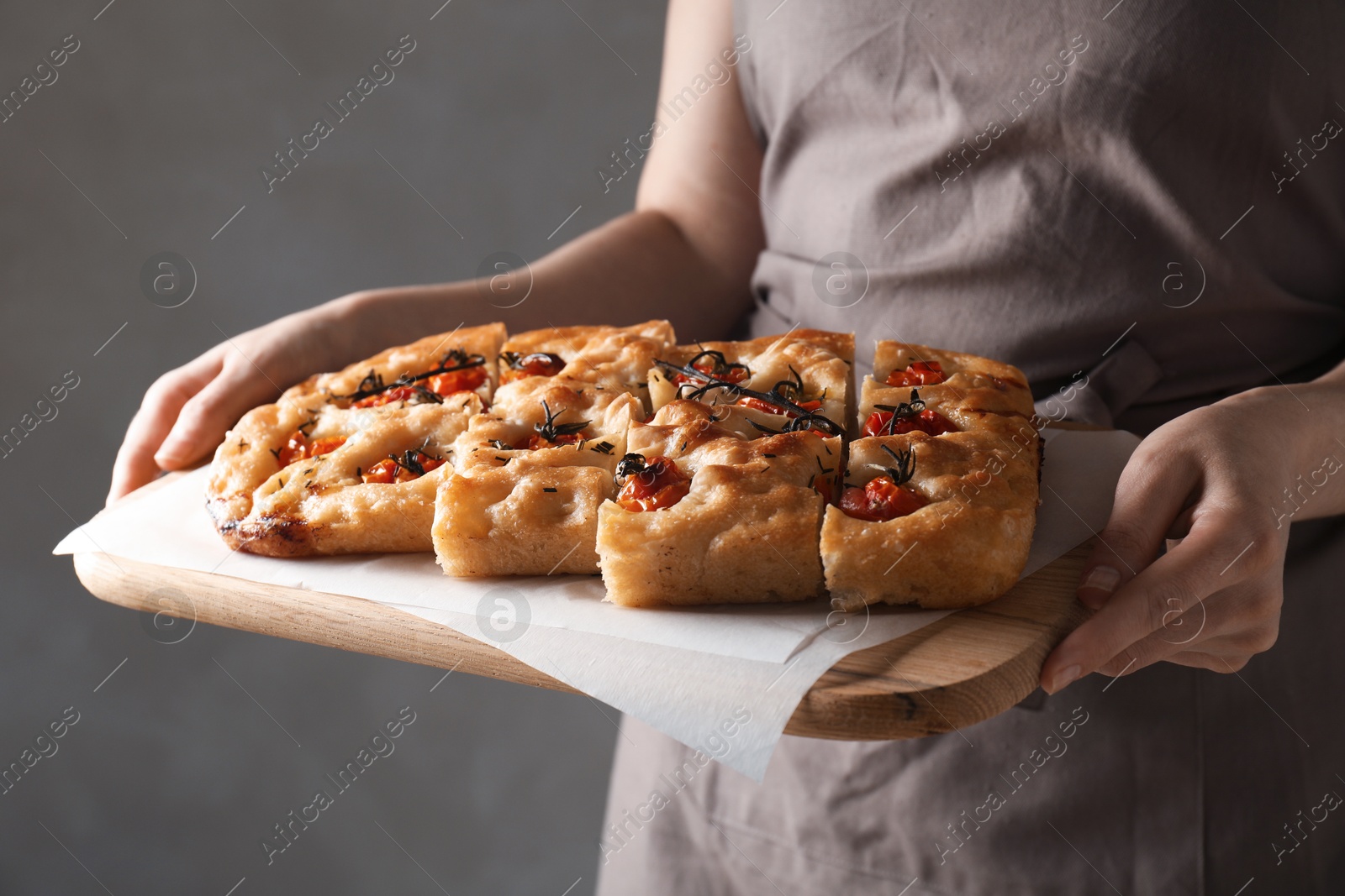 Photo of Woman holding cut delicious focaccia with tomatoes and spices on gray background, closeup