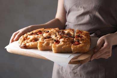 Photo of Woman holding cut delicious focaccia with tomatoes and spices on gray background, closeup