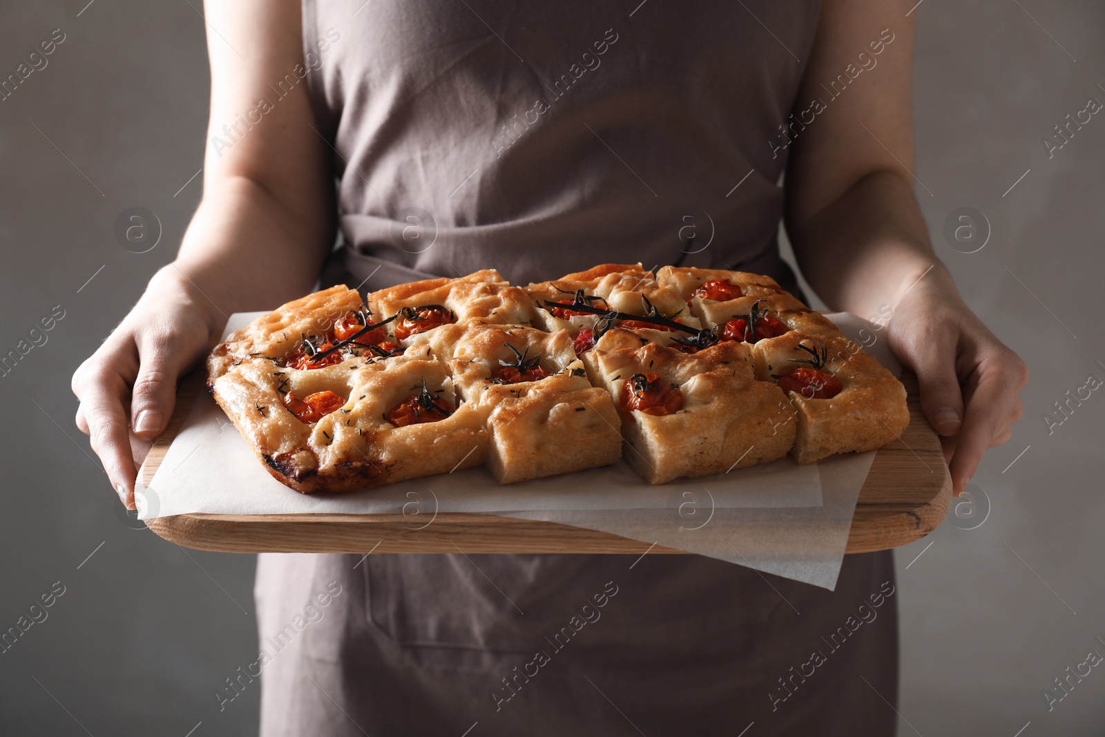 Woman holding cut delicious focaccia with tomatoes and spices on gray background, closeup Photo of Woman holding cut delicious focaccia with tomatoes and spices on gray background, closeup