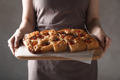 Photo of Woman holding cut delicious focaccia with tomatoes and spices on gray background, closeup