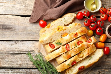 Photo of Cut delicious focaccia with tomatoes, spices and oil on wooden table, flat lay. Space for text