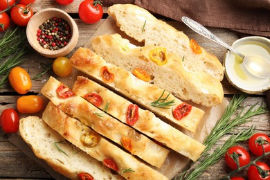 Photo of Cut delicious focaccia with tomatoes, spices and oil on wooden table, flat lay