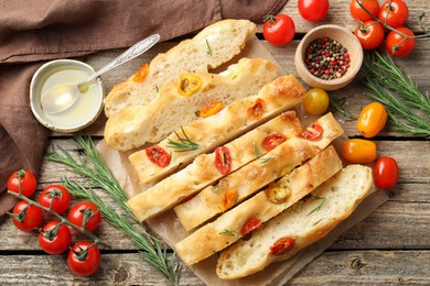 Photo of Cut delicious focaccia with tomatoes, spices and oil on wooden table, flat lay