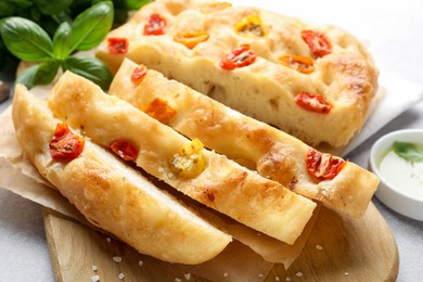 Photo of Cut delicious focaccia with tomatoes and basil on table, closeup