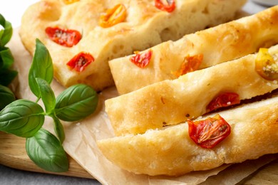 Photo of Cut delicious focaccia with tomatoes and basil on table, closeup