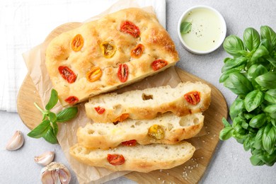 Photo of Cut delicious focaccia with tomatoes, spices and oil on gray table, flat lay
