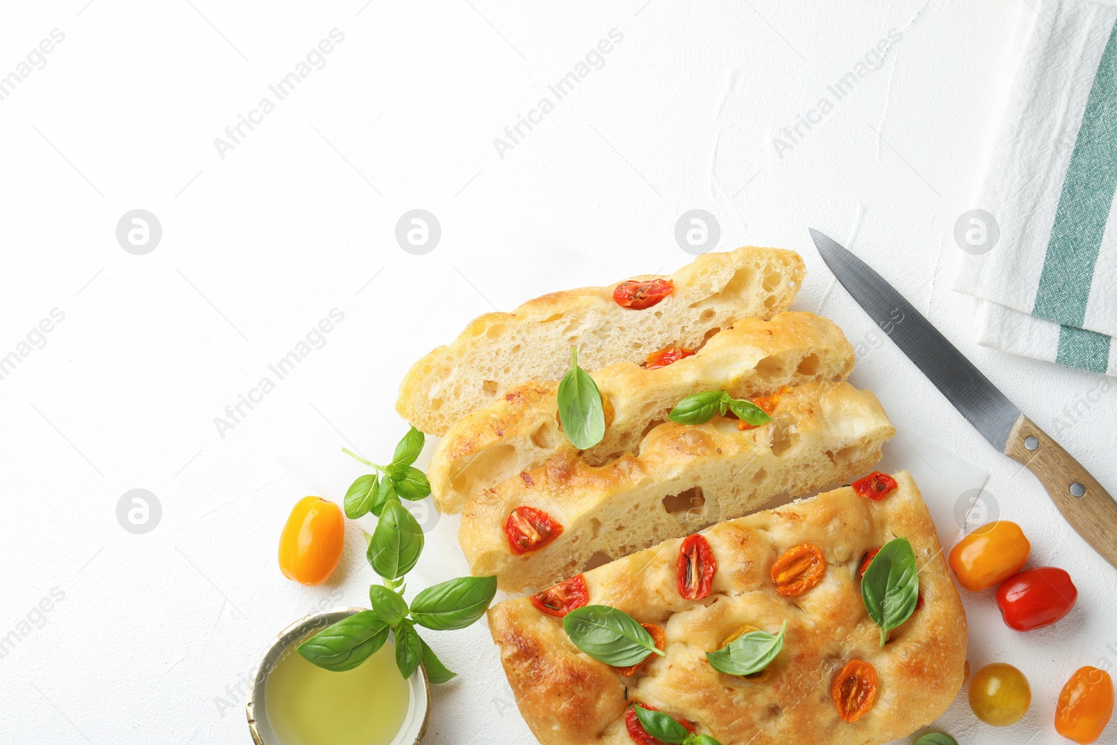 Cut delicious focaccia with tomatoes, basil, oil and knife on light table, flat lay. Space for text Photo of Cut delicious focaccia with tomatoes, basil, oil and knife on light table, flat lay. Space for text