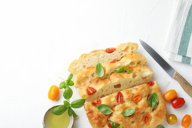 Photo of Cut delicious focaccia with tomatoes, basil, oil and knife on light table, flat lay. Space for text