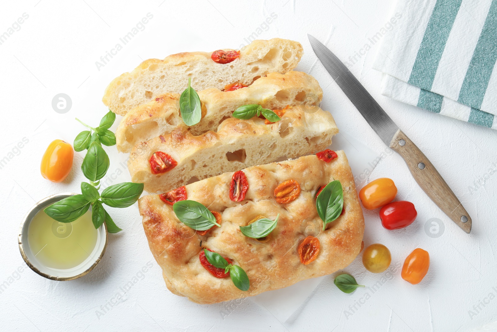 Cut delicious focaccia with tomatoes, basil, oil and knife on light table, flat lay Photo of Cut delicious focaccia with tomatoes, basil, oil and knife on light table, flat lay