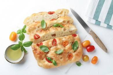 Photo of Cut delicious focaccia with tomatoes, basil, oil and knife on light table, flat lay
