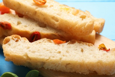 Photo of Pieces of delicious focaccia with tomatoes on light blue table, closeup