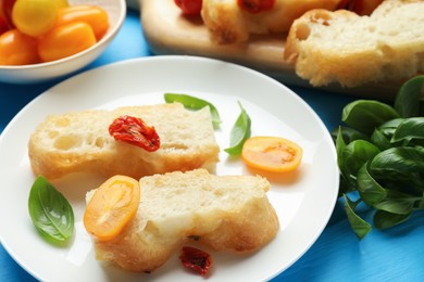 Photo of Pieces of delicious focaccia with tomatoes and basil on light blue wooden table, closeup
