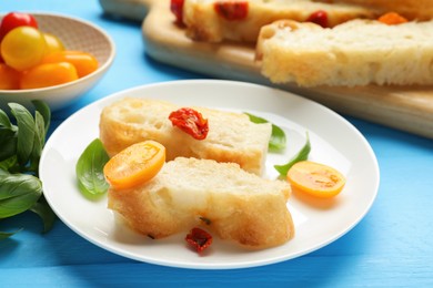 Photo of Pieces of delicious focaccia with tomatoes and basil on light blue wooden table, closeup