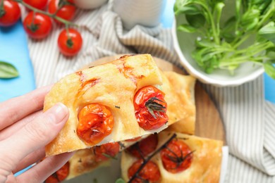 Photo of Woman holding piece of delicious focaccia with tomatoes at table, top view