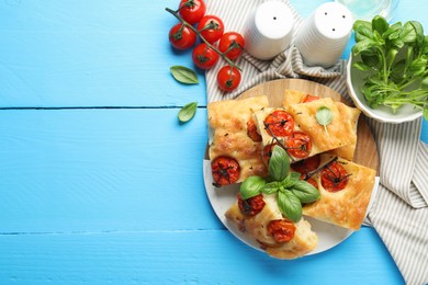 Photo of Pieces of delicious focaccia with tomatoes and spices on light blue wooden table, flat lay. Space for text
