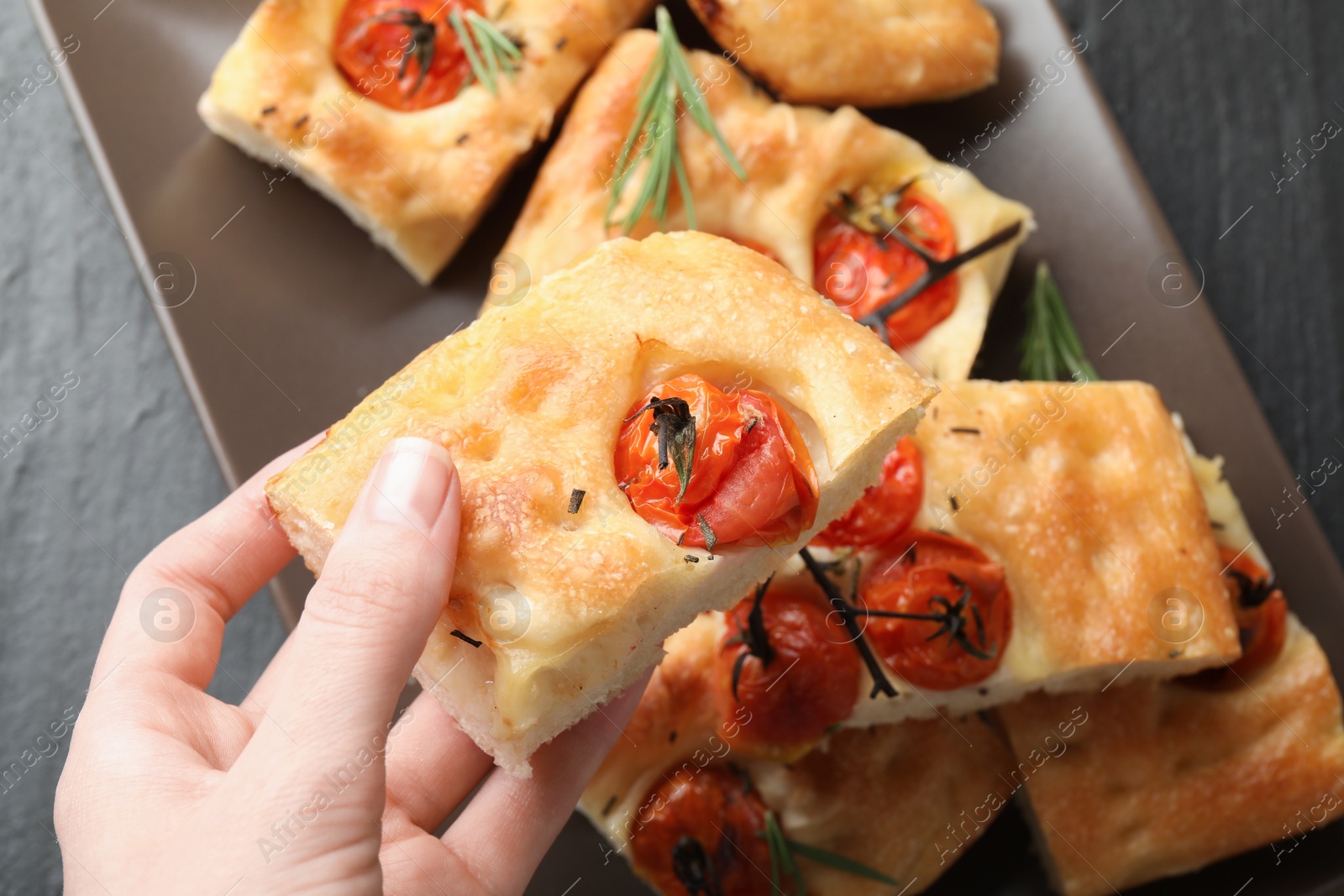 Woman holding piece of delicious focaccia with tomatoes and spices at table, top view Photo of Woman holding piece of delicious focaccia with tomatoes and spices at table, top view