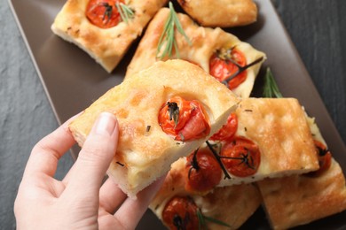 Photo of Woman holding piece of delicious focaccia with tomatoes and spices at table, top view